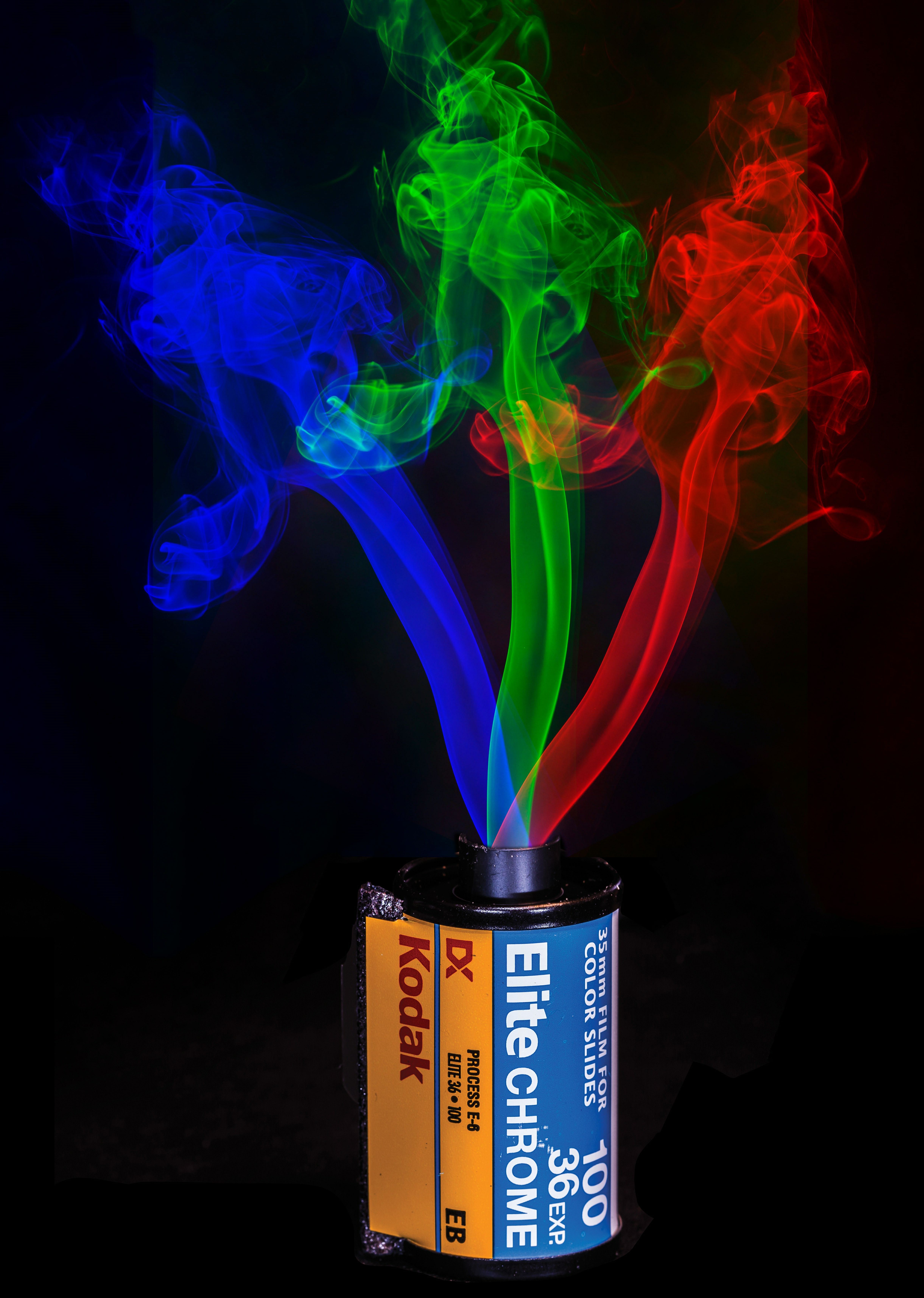 Red, green, and blue smoke rising from a canister of Kodak Elite Chrome 35mm film against a black background.