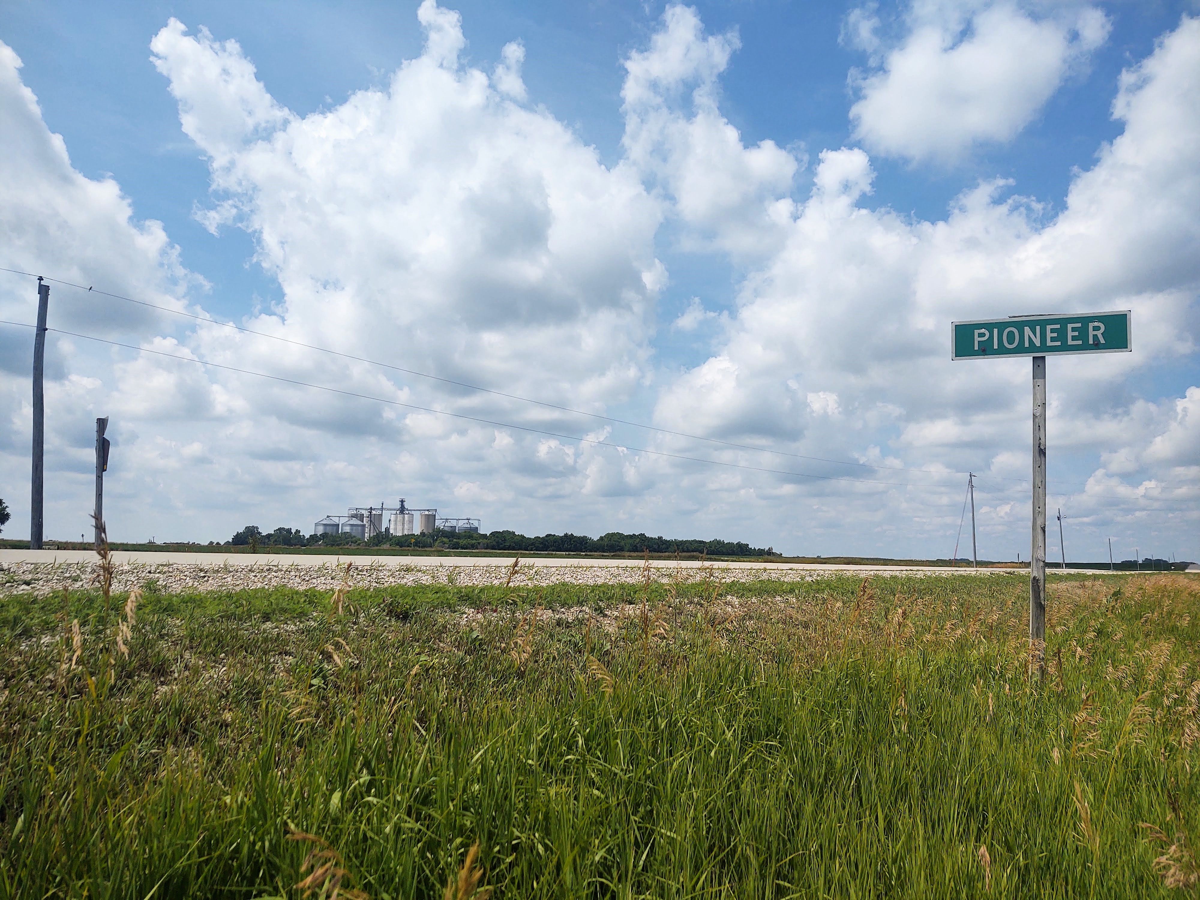 Photograph of a rural highway. A sign in the foreground simply says PIONEER.
